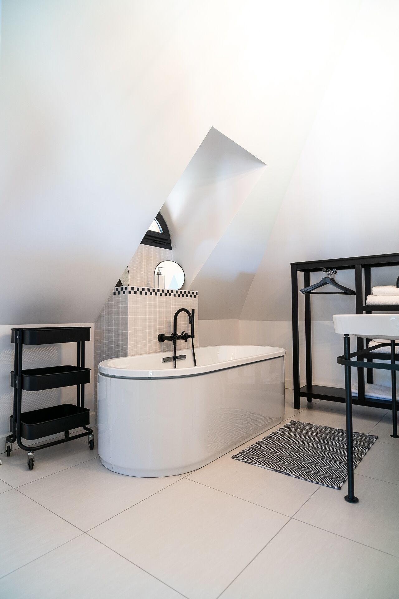 Een moderne badkamer met een vrijstaand bad, een zwarte metalen plankkast en een ophangrek voor handdoeken.