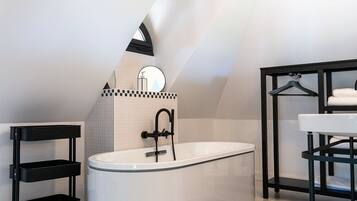 Een moderne badkamer met een vrijstaand bad, een zwarte metalen plankkast en een ophangrek voor handdoeken.