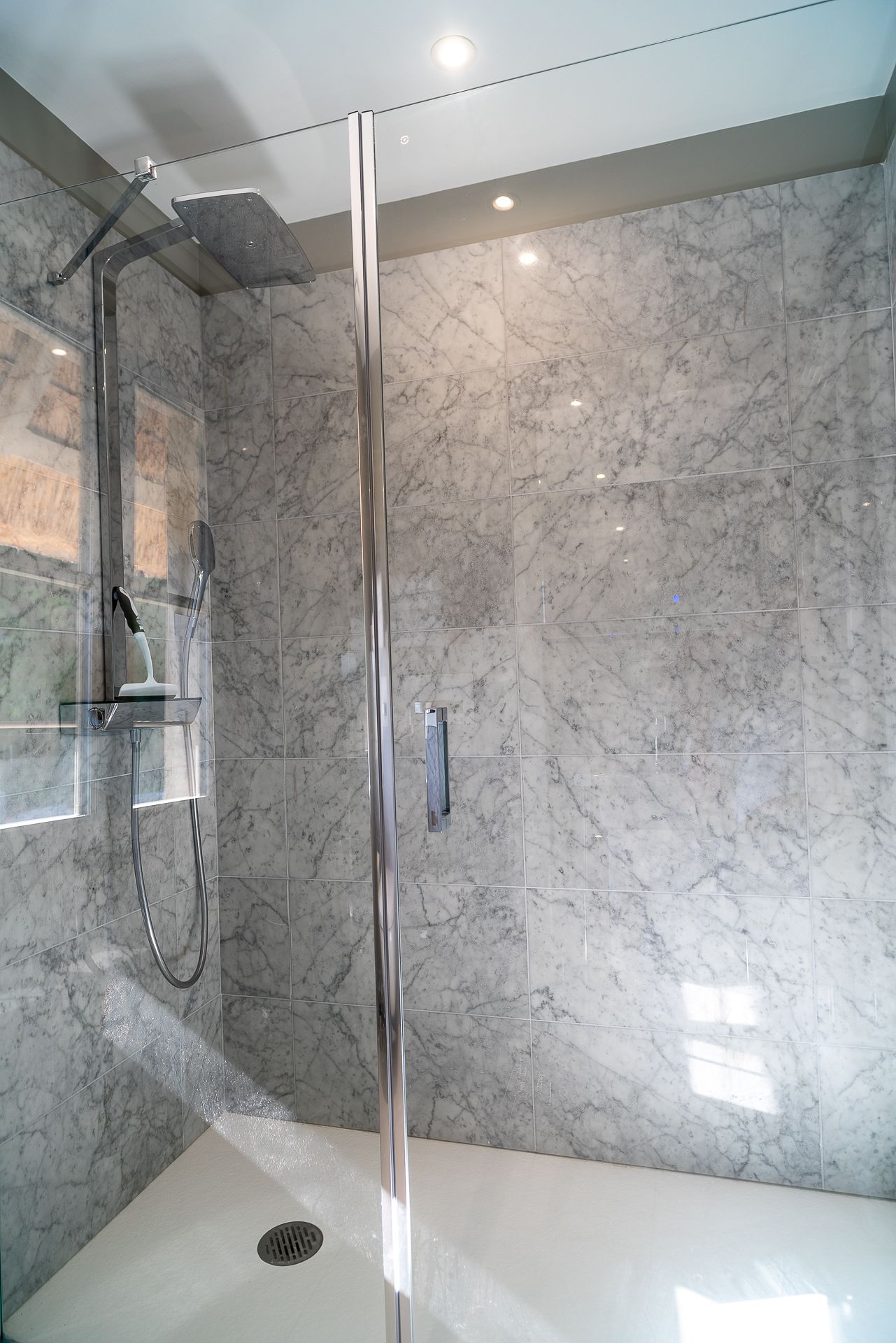 A modern bathroom with a glass shower enclosure, marble walls, and a built-in toilet.
