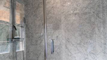 A modern bathroom with a glass shower enclosure, marble walls, and a built-in toilet.