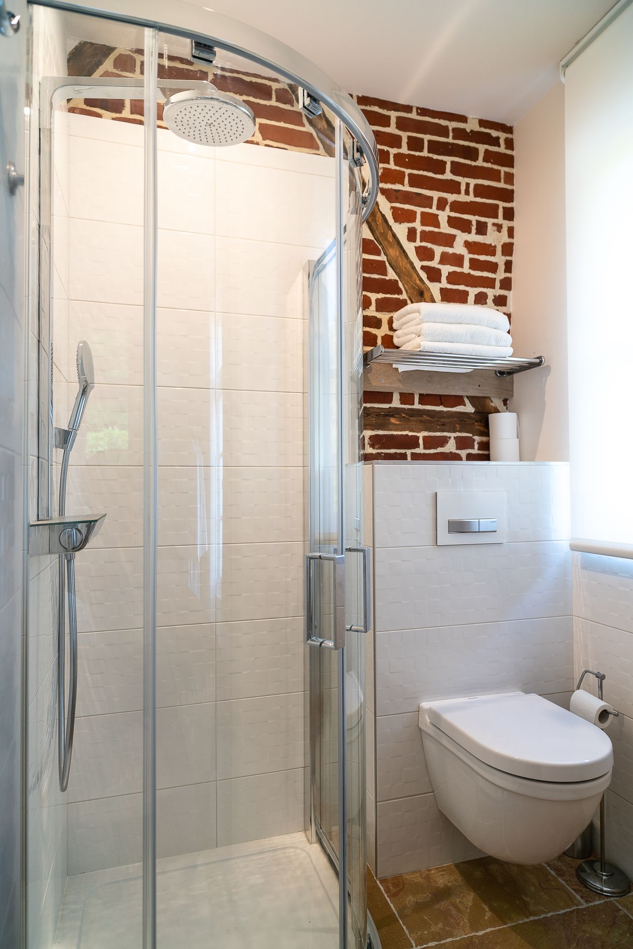 Un baño moderno con cabina de ducha de vidrio, inodoro blanco y pared de ladrillo decorativa.