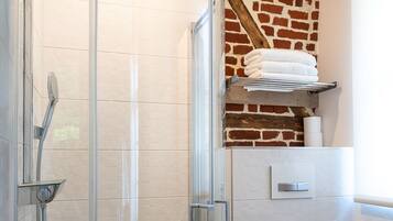 Un baño moderno con cabina de ducha de vidrio, inodoro blanco y pared de ladrillo decorativa.