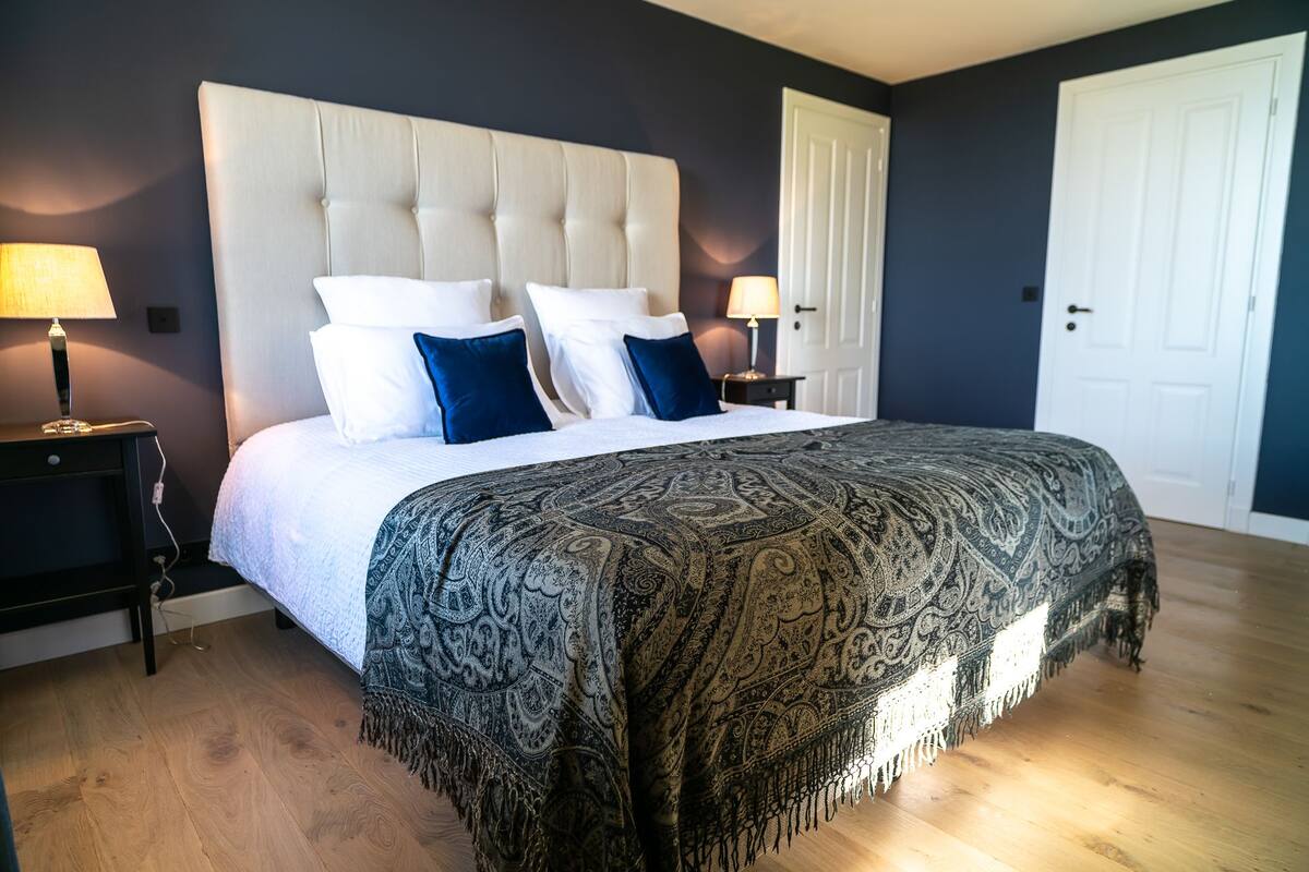 Un dormitorio con una cama grande, dos mesitas de noche y una puerta.