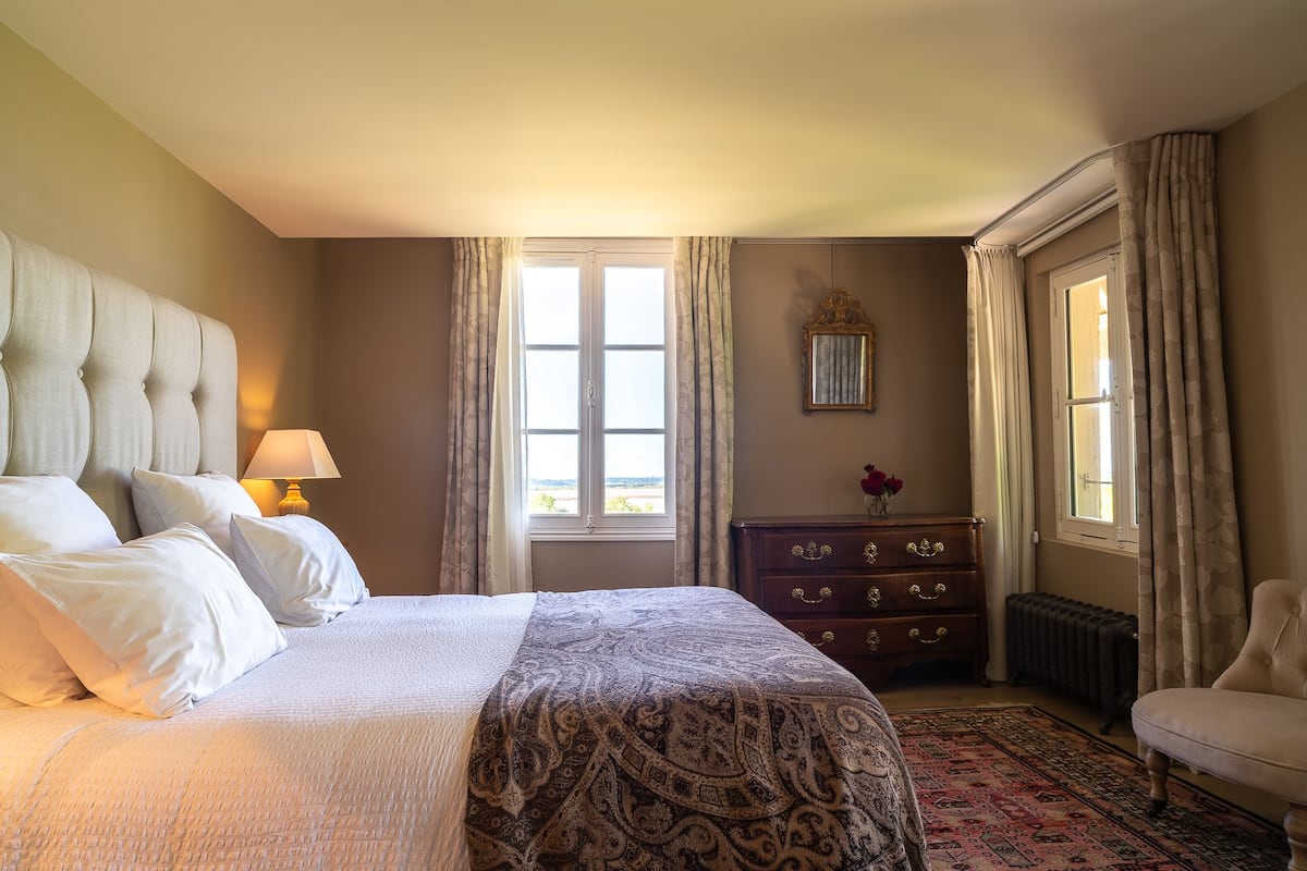 Un dormitorio con una cama grande, un aparador, una silla y una ventana con cortinas.