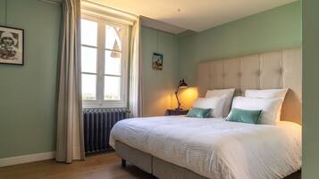 Une chambre à coucher avec un grand lit, une fenêtre avec des rideaux, un radiateur et une table de chevet avec une lampe.