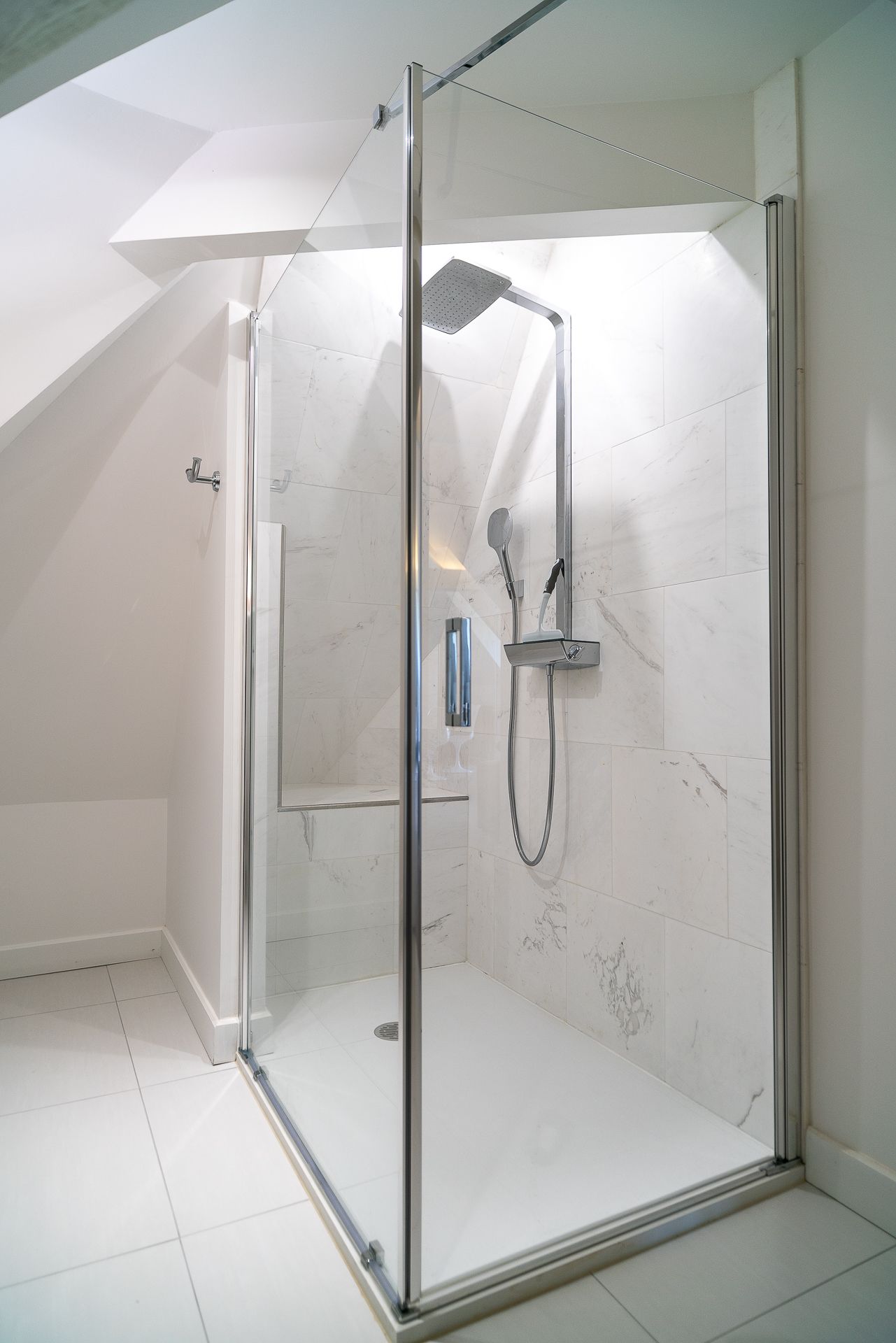 A modern glass-enclosed shower with a handheld showerhead and a wall-mounted faucet.