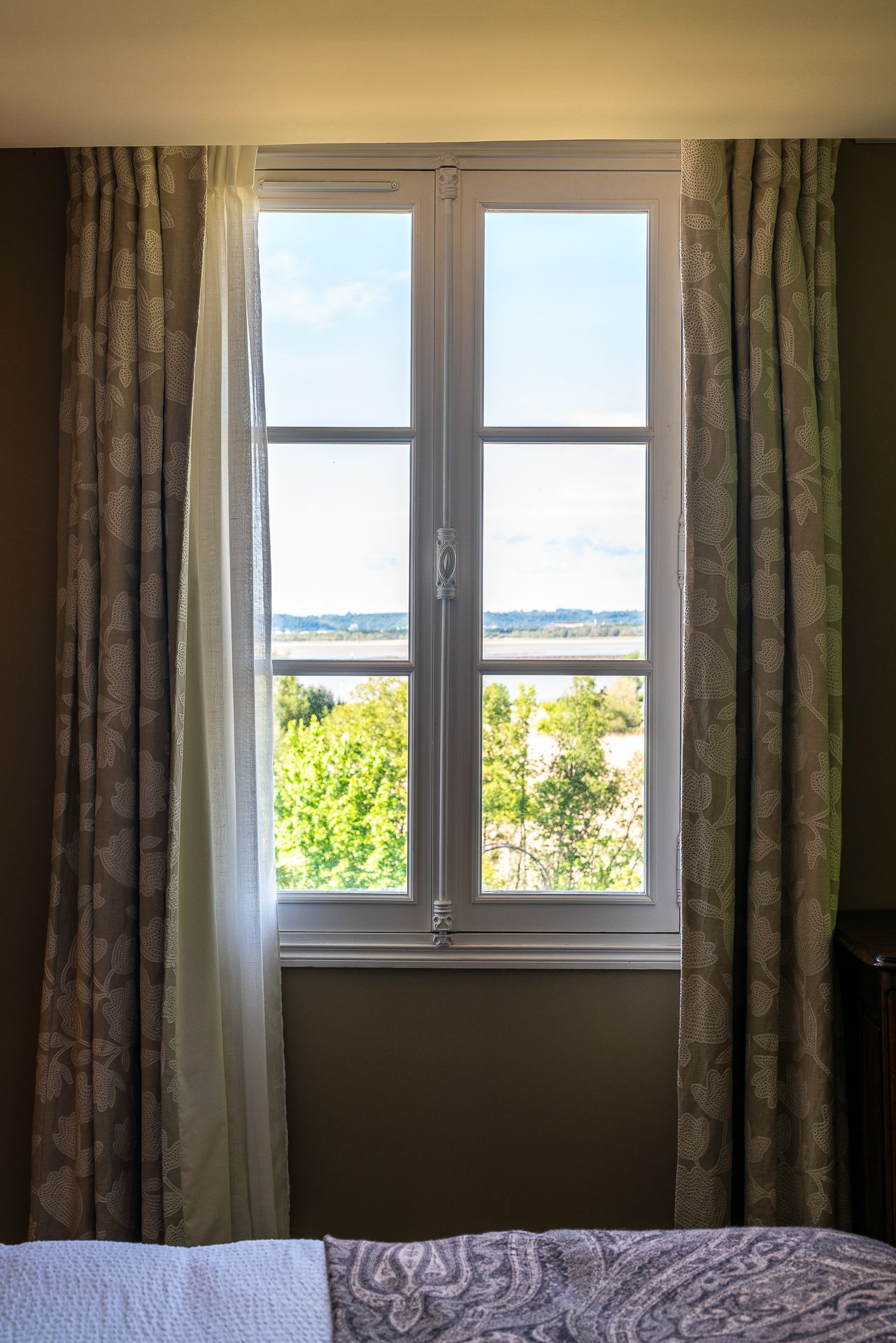 Une pièce avec une grande fenêtre, des rideaux et un lit.