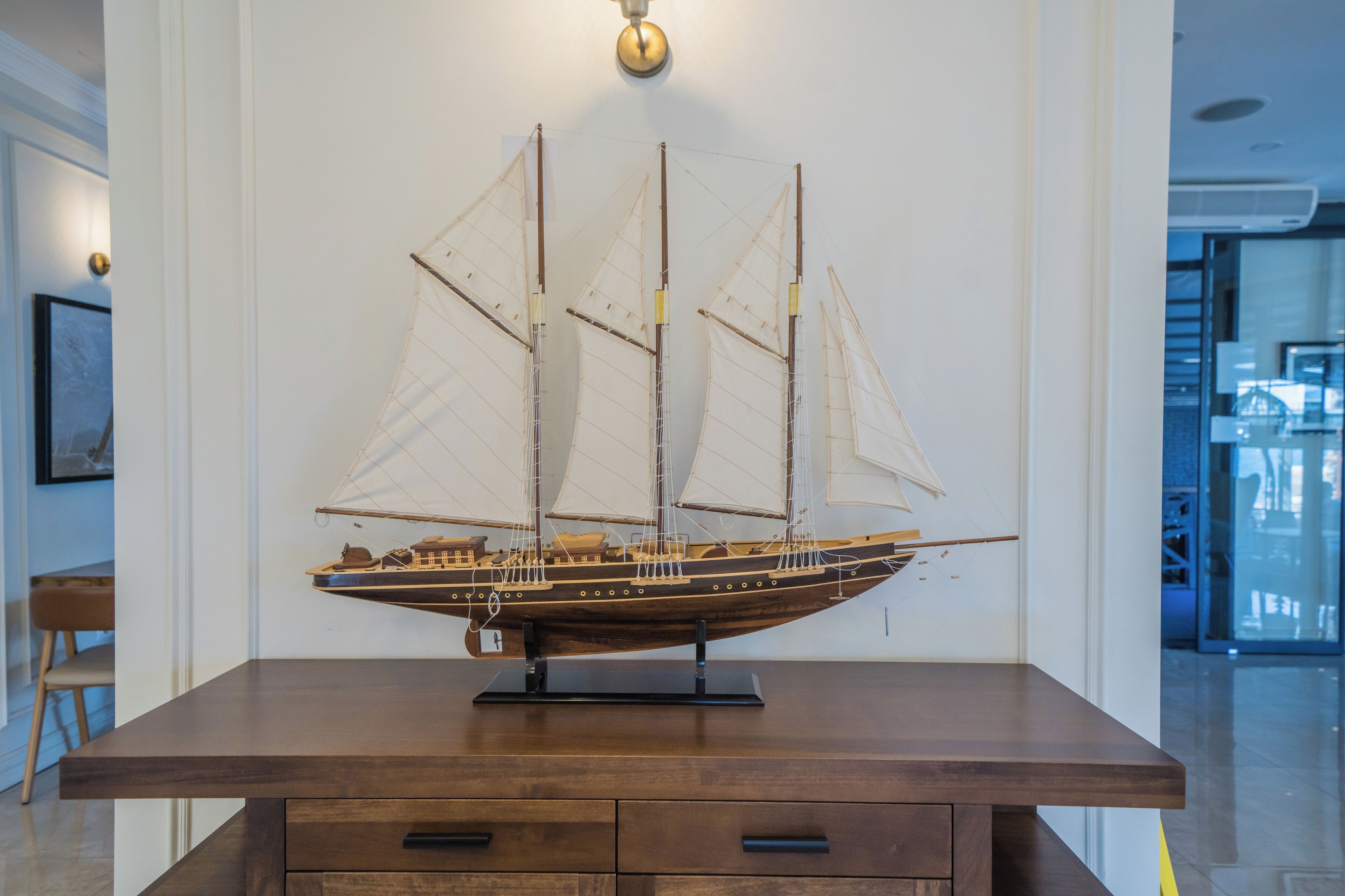 A model ship on a wooden table in a room with white walls and a ceiling light.