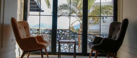 Deux chaises sont placées face à une grande fenêtre donnant sur des palmiers et un balcon.