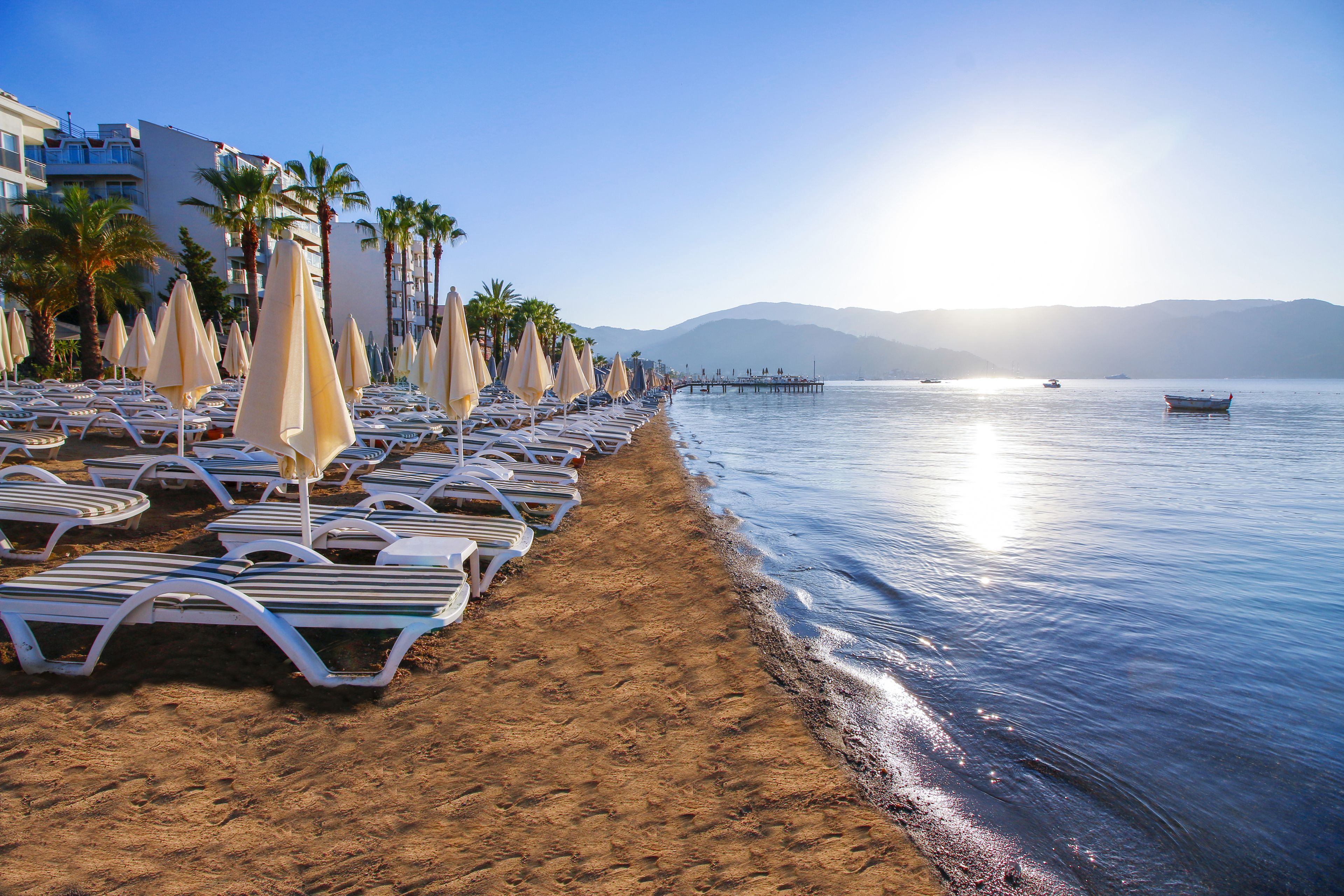 A beach with rows of sun loungers and umbrellas, a pier extending into the water, and a clear sky.