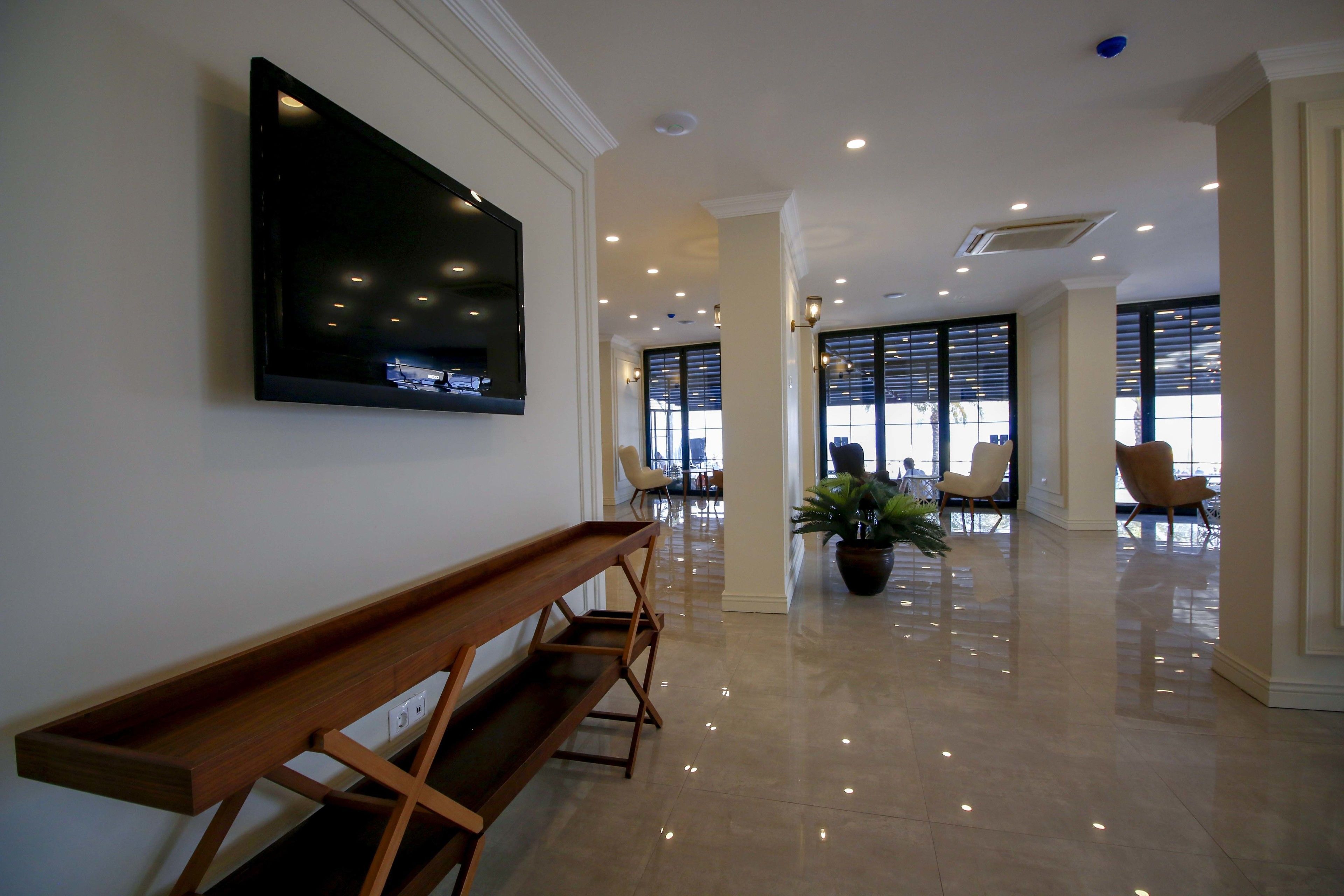 A spacious lobby with a wooden bench, a mounted TV, and a potted plant.