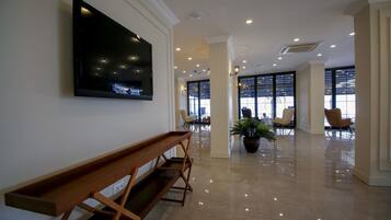 A spacious lobby with a wooden bench, a mounted TV, and a potted plant.