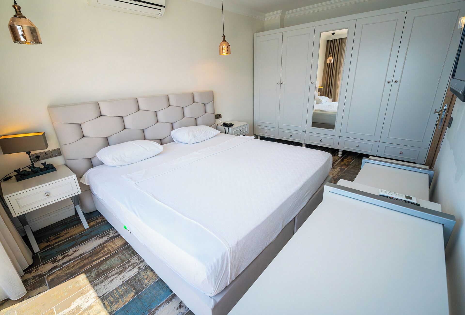 Una camera d'albergo con un letto grande, un comodino con una lampada, un armadio e una scrivania con un computer.