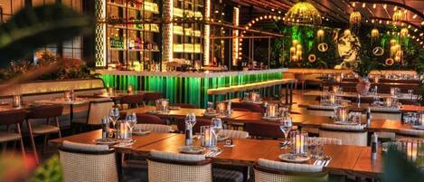 A restaurant with multiple dining tables, wicker chairs, and hanging light fixtures.