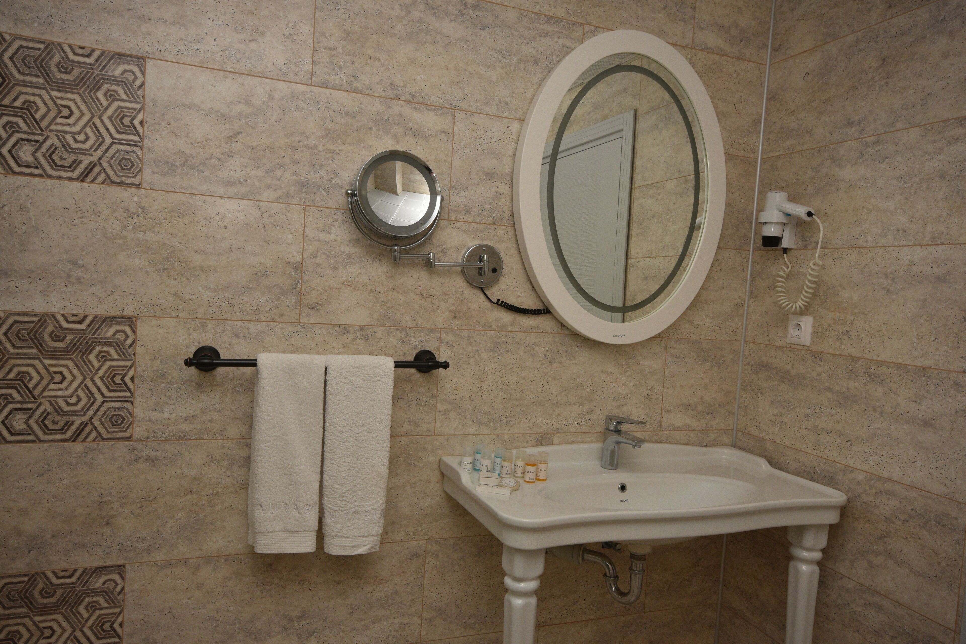 Un baño con lavamanos, espejo, toallero y azulejos estampados.