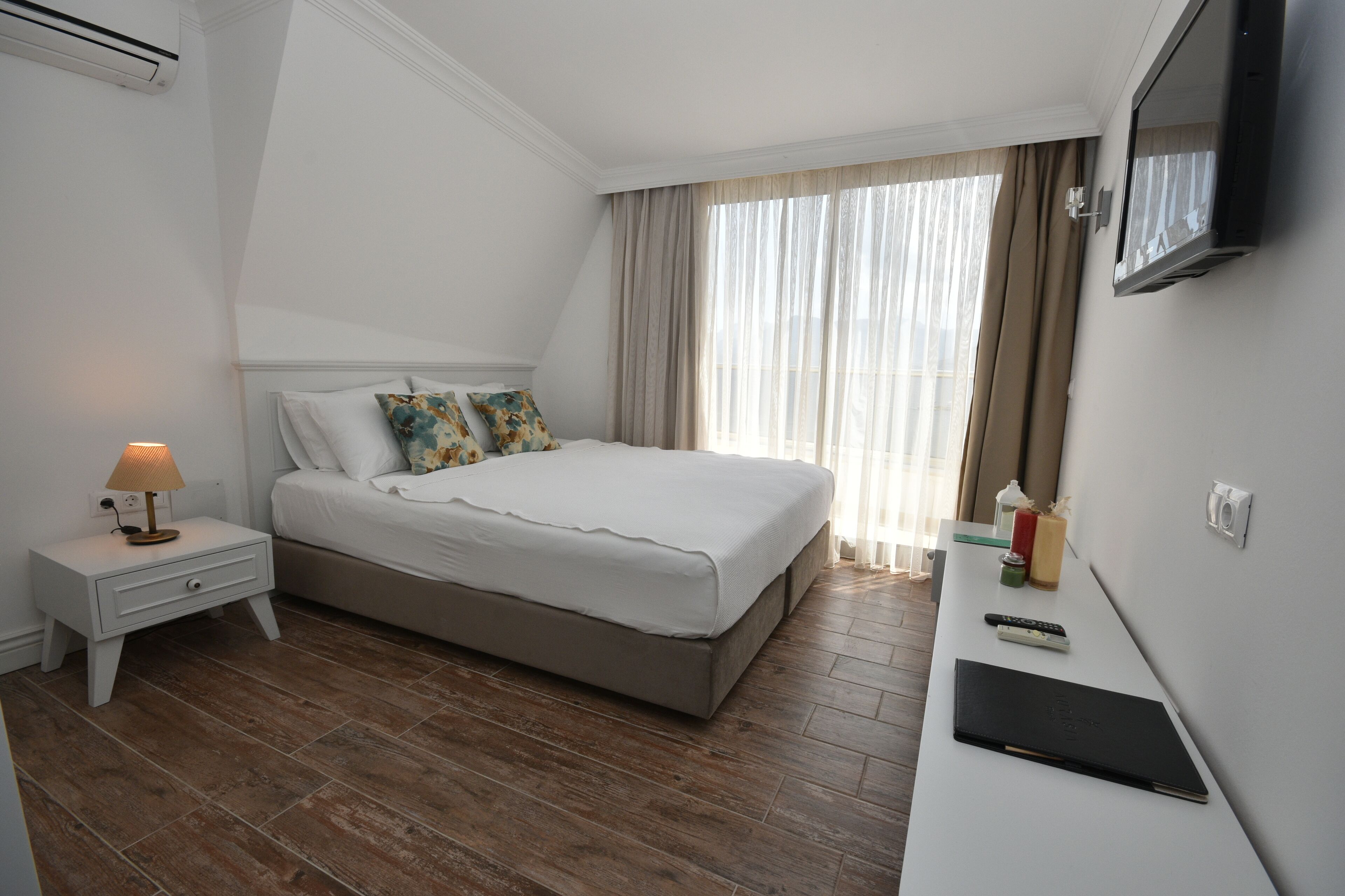 A hotel room with a bed, a nightstand, a desk, a TV, and a window with curtains.