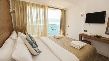A hotel room with a bed, a desk, a TV, and a view of the sea.