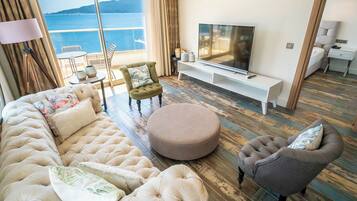 A living room with a large sofa, ottoman, armchair, TV, and a view of the sea.
