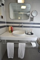 Un baño con lavamanos blanco, un espejo y dos toallas colgadas de ganchos.