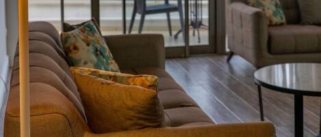 A modern living room with a sofa, a coffee table, and a lamp. There is a view of the sea through large windows.