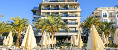 A hotel named "AURASIA" with multiple balconies, sun loungers, and palm trees in the foreground.
