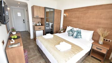 Habitación de hotel con una cama grande, cabecera de madera, un escritorio con espejo, un televisor y una kitchenette pequeña.