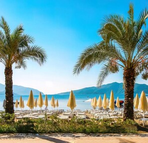 A beachside resort with rows of sun loungers and umbrellas, palm trees, and a view of the sea and mountains in the background. - Aurasia Beach Hotel (Marmaris)