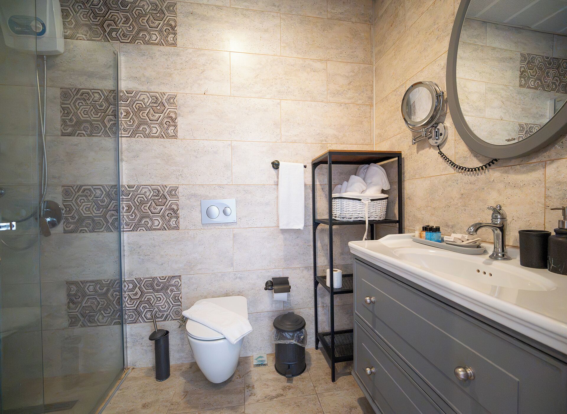 A bathroom with a glass shower enclosure, a toilet, a vanity with a mirror, and patterned tiles on the walls.