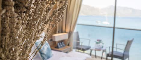 Un dormitorio con cama, mesita de noche, lámpara, silla y vistas al mar a través de amplias ventanas.