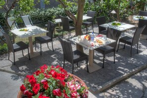 Un café en plein air, avec des tables et des chaises, entouré de verdure.