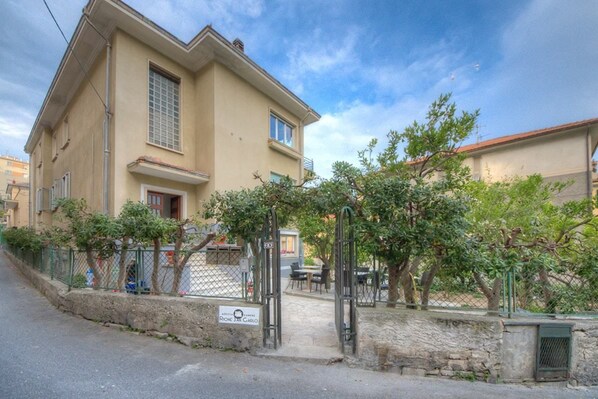 Un bâtiment à deux étages, doté d’une façade beige, d’une entrée sécurisée par un portail et d’un petit patio aménagé avec des sièges extérieurs.
