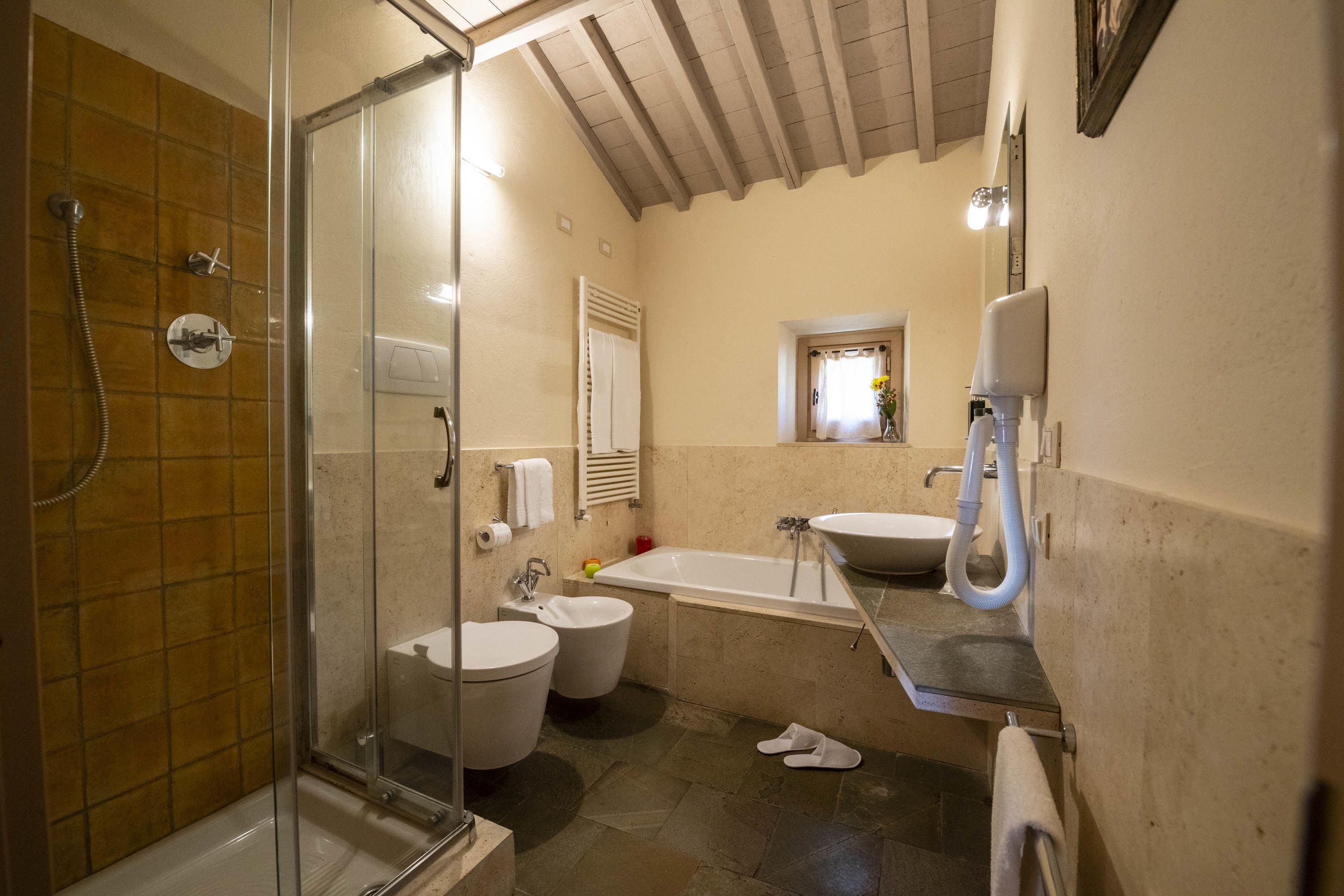 A bathroom with a glass-enclosed shower, two toilets, a bathtub, and a sink.