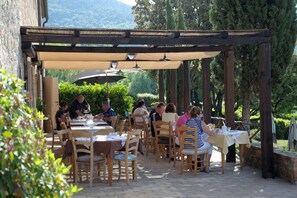 An outdoor patio with wooden tables and chairs, covered by a pergola with umbrellas. - Il Defizio (Gambassi Terme)