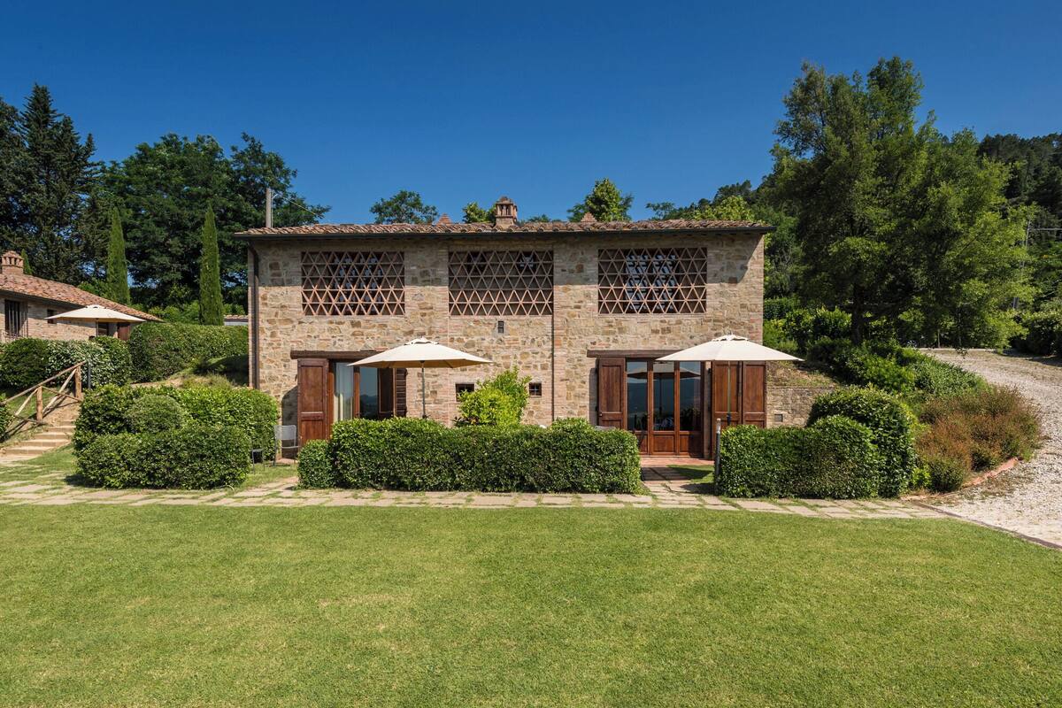 A stone building with a tiled roof, two large windows with shutters, and a well-maintained lawn.