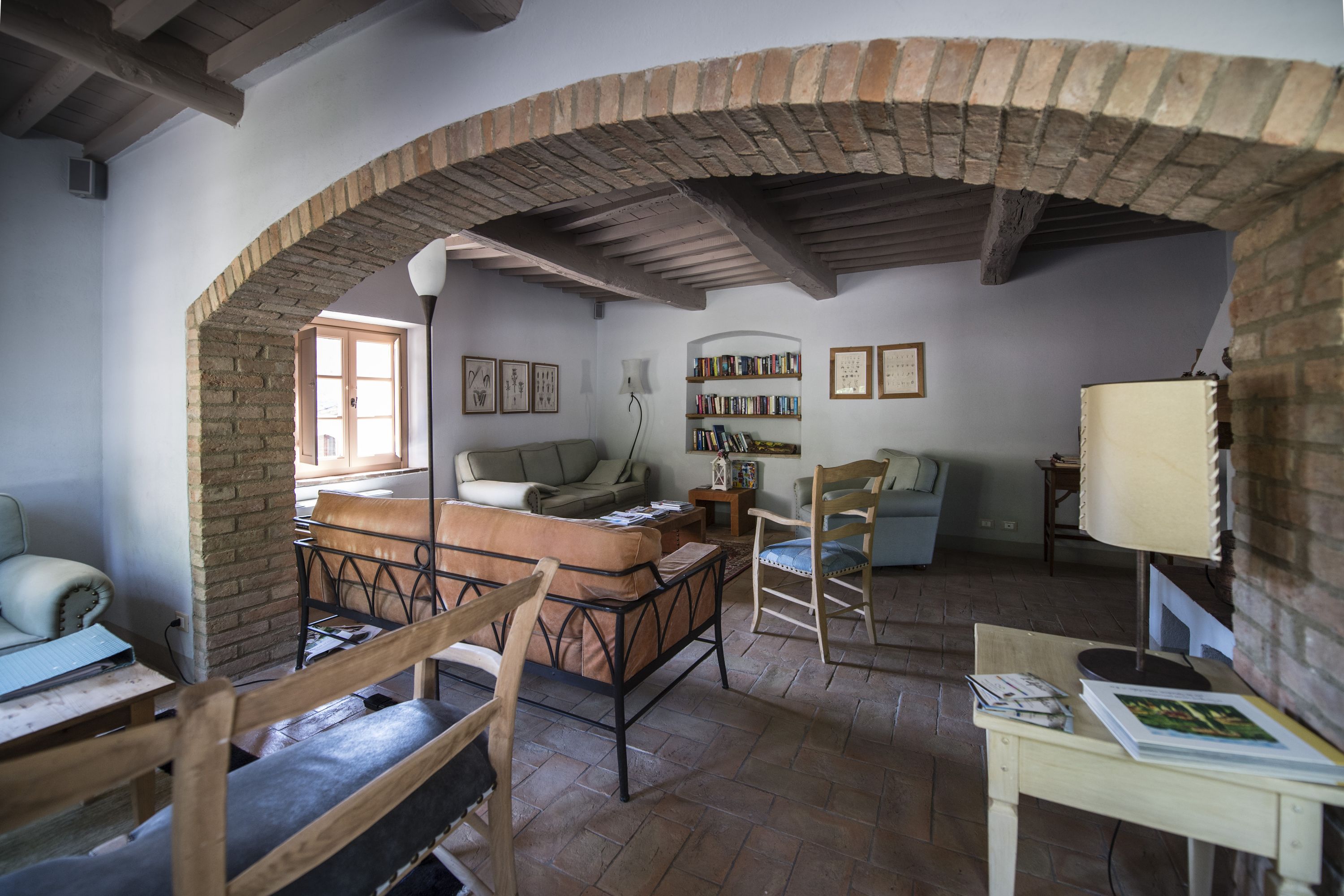 Una habitación acogedora con un arco de ladrillo, un sofá, una silla de madera, una mesa con libros y una lámpara.