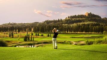 Ein Golfplatz mit einem Spieler im Schwung, einem Schloss auf einem Hügel und einem klaren Himmel.