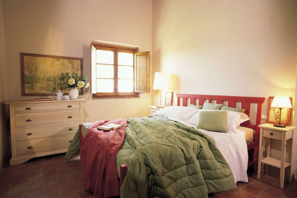 A bedroom with a bed, a dresser, a nightstand, a window, and a painting on the wall.