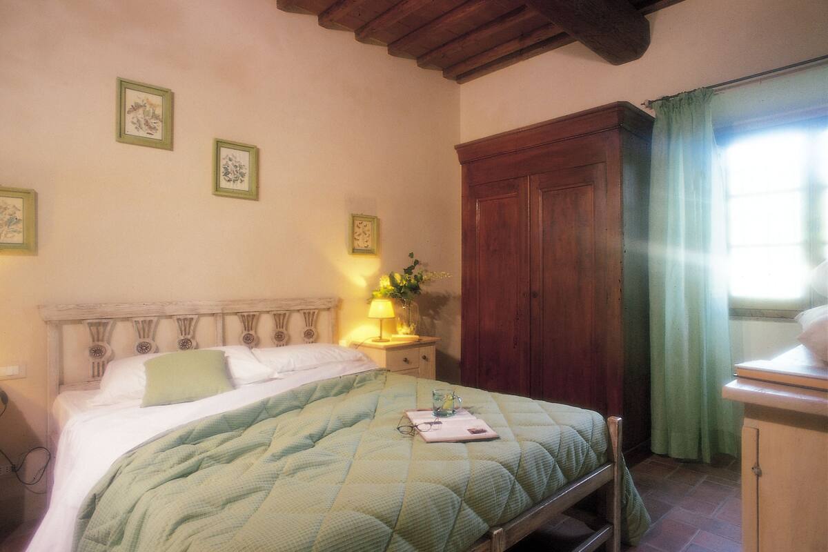 A bedroom with a bed, a nightstand with a lamp, a wooden wardrobe, and framed pictures on the wall.