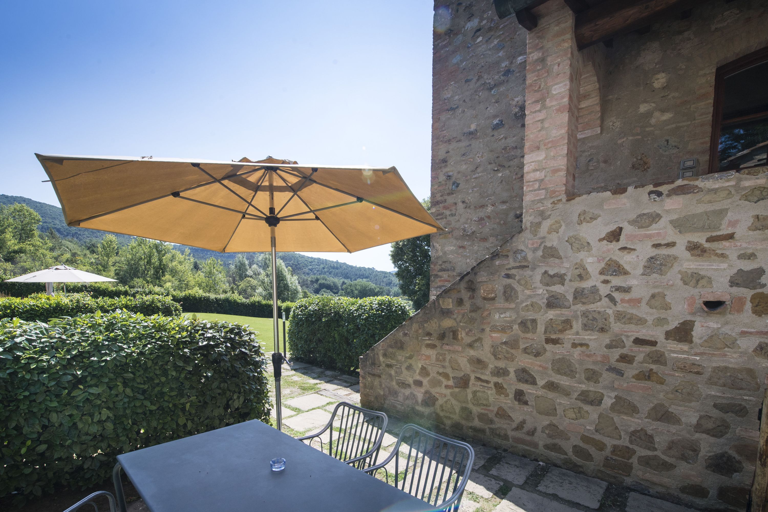 An outdoor patio with a table and chairs, a large umbrella, and a stone wall.