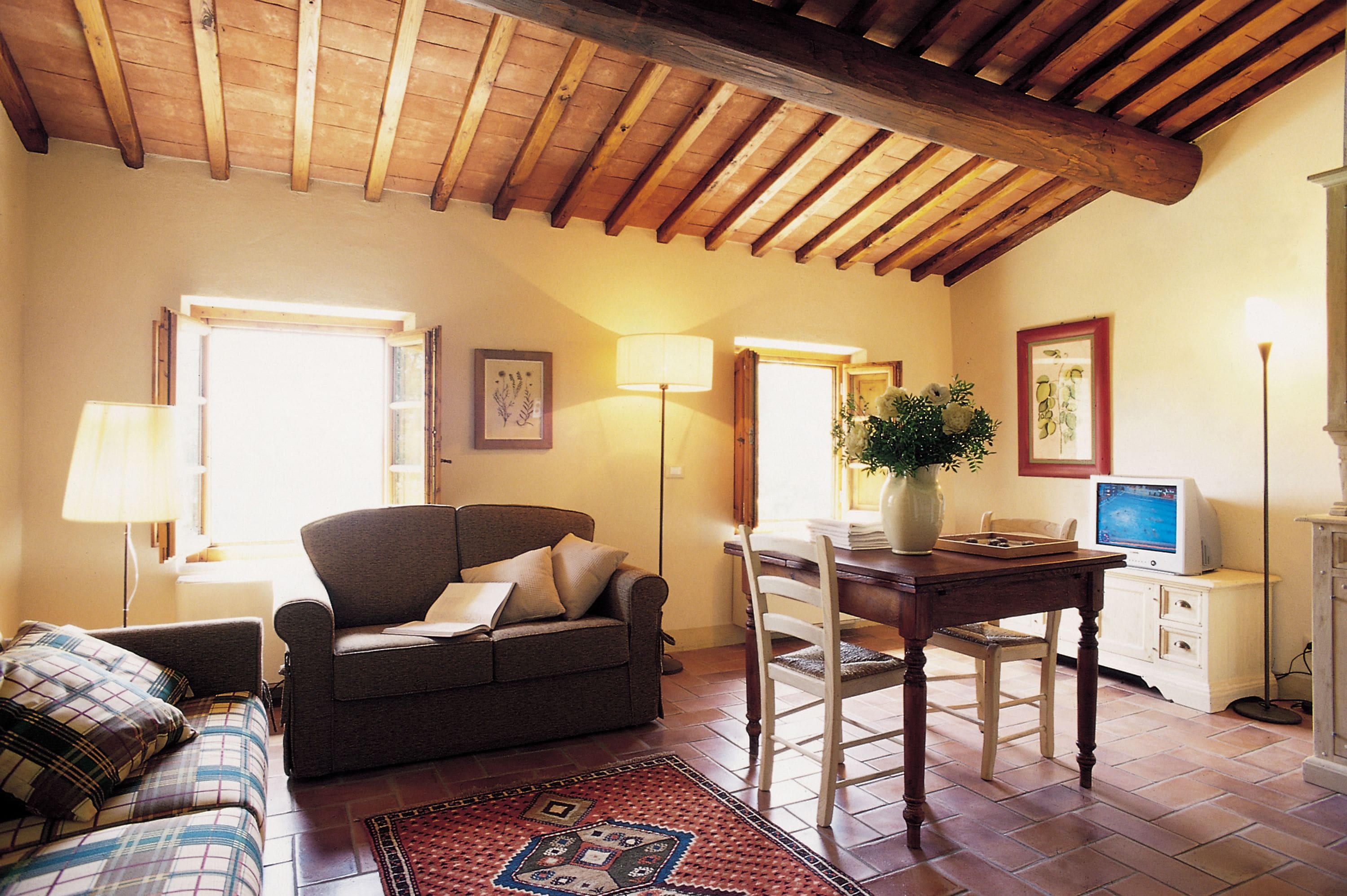 Un salon chaleureux avec un plafond en bois, un canapé, une table à manger avec des chaises, un téléviseur et une lampe.