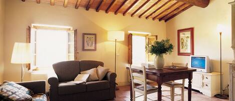 Un salon chaleureux avec un plafond en bois, un canapé, une table à manger avec des chaises, un téléviseur et une lampe.