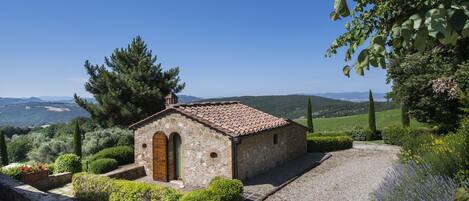 A small stone building with a tiled roof, surrounded by well-maintained gardens and a gravel path.
