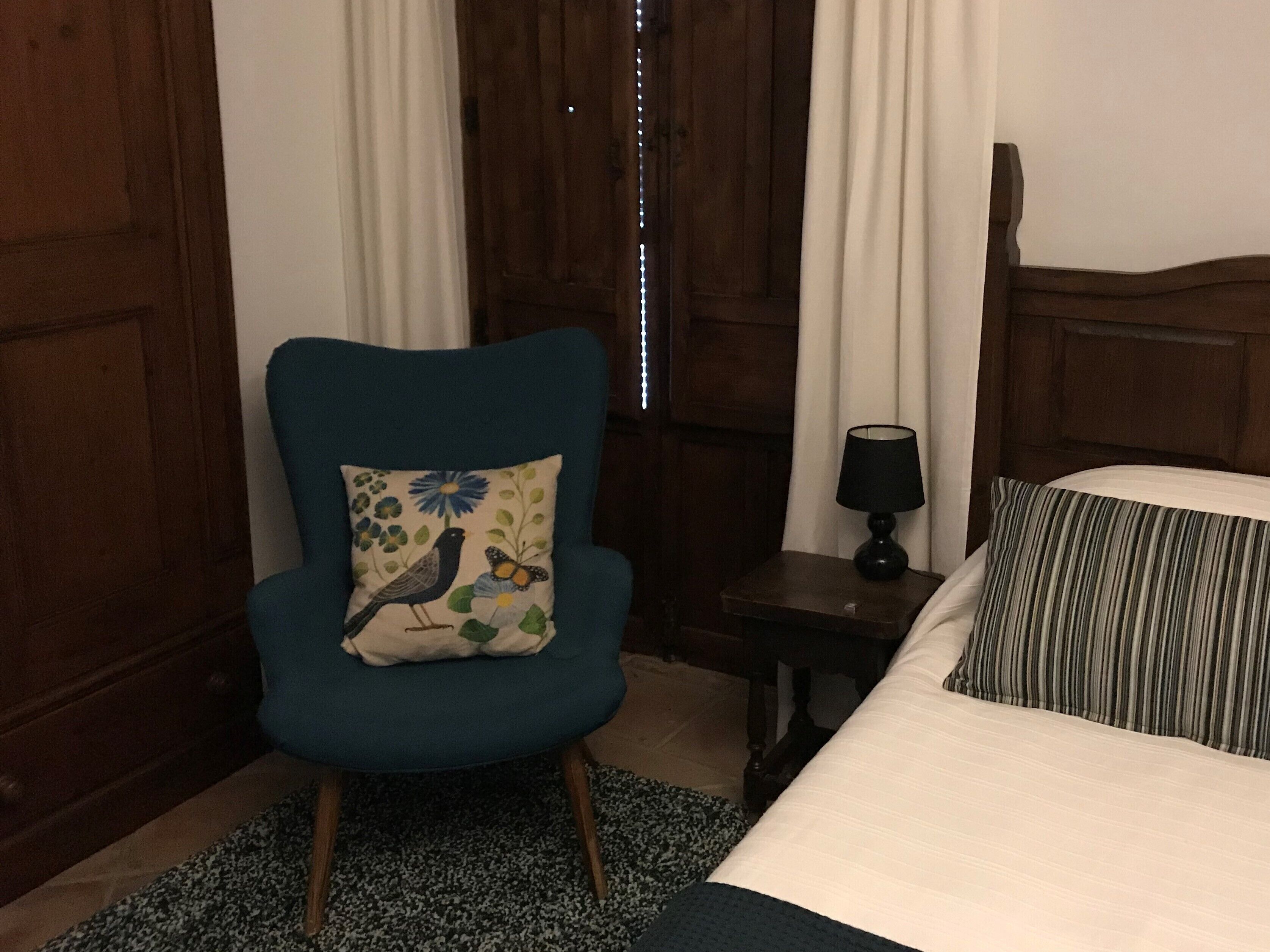 Une pièce comprenant un lit, une chaise avec un coussin à motifs floraux, une petite table avec une lampe et des murs en bois.
