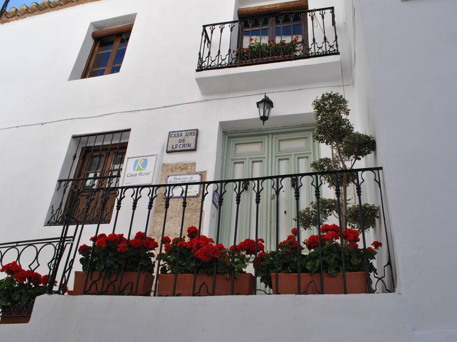 A white building with a balcony, a door, and a window. There are signs on the wall and flowers in the balcony.