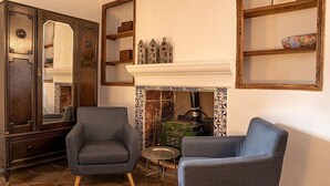 Una habitación con dos sillones grises, un mueble de madera con espejo y una chimenea con zócalo de azulejos.