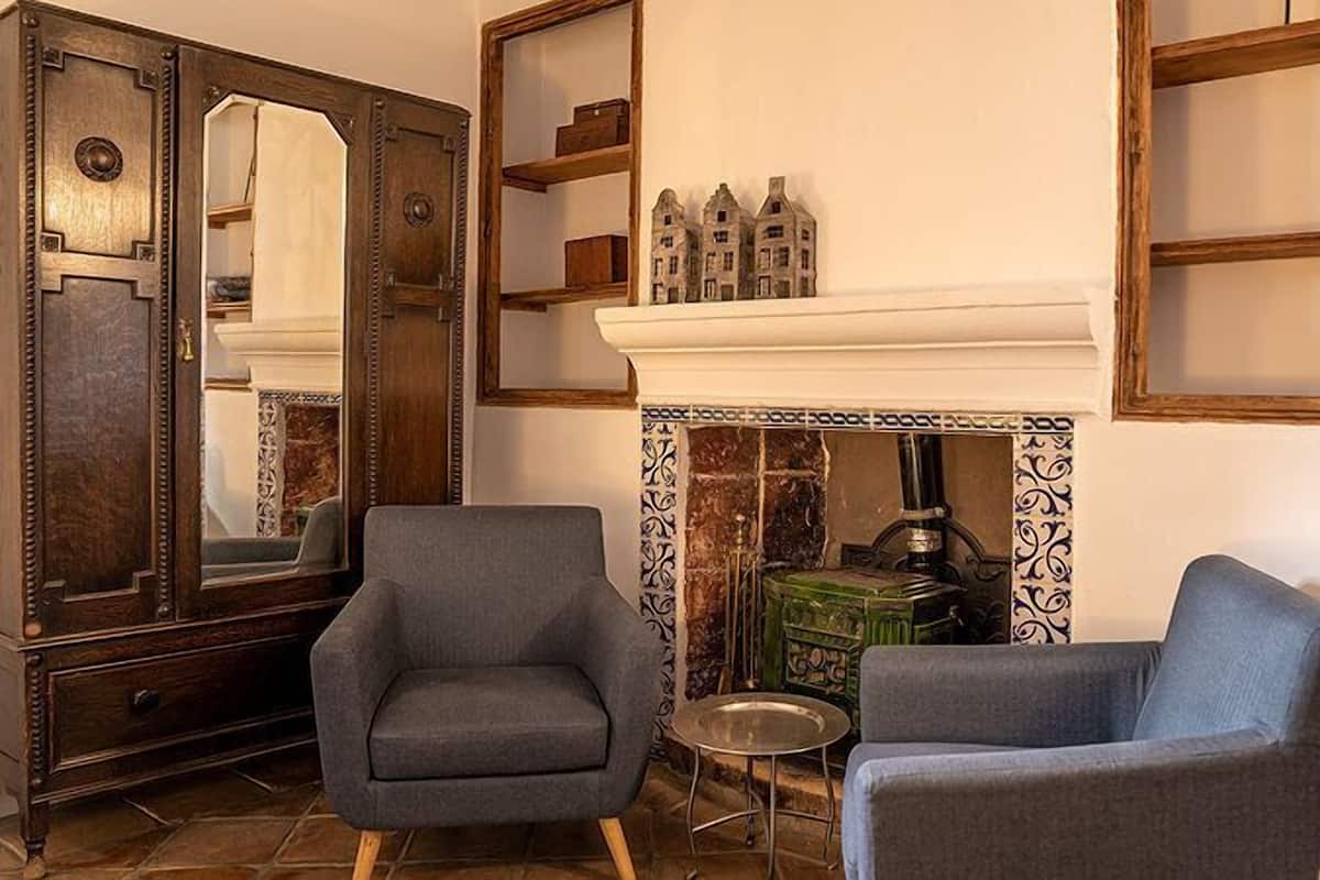 A room with two grey armchairs, a wooden cabinet with a mirror, and a fireplace with a tiled surround.