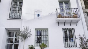 Un edificio blanco con un letrero que indica que es un hospedaje. Hay plantas en macetas y un banco afuera.