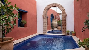 Una piscina con borde de azulejos, rodeada de muros rojos y un arco blanco.