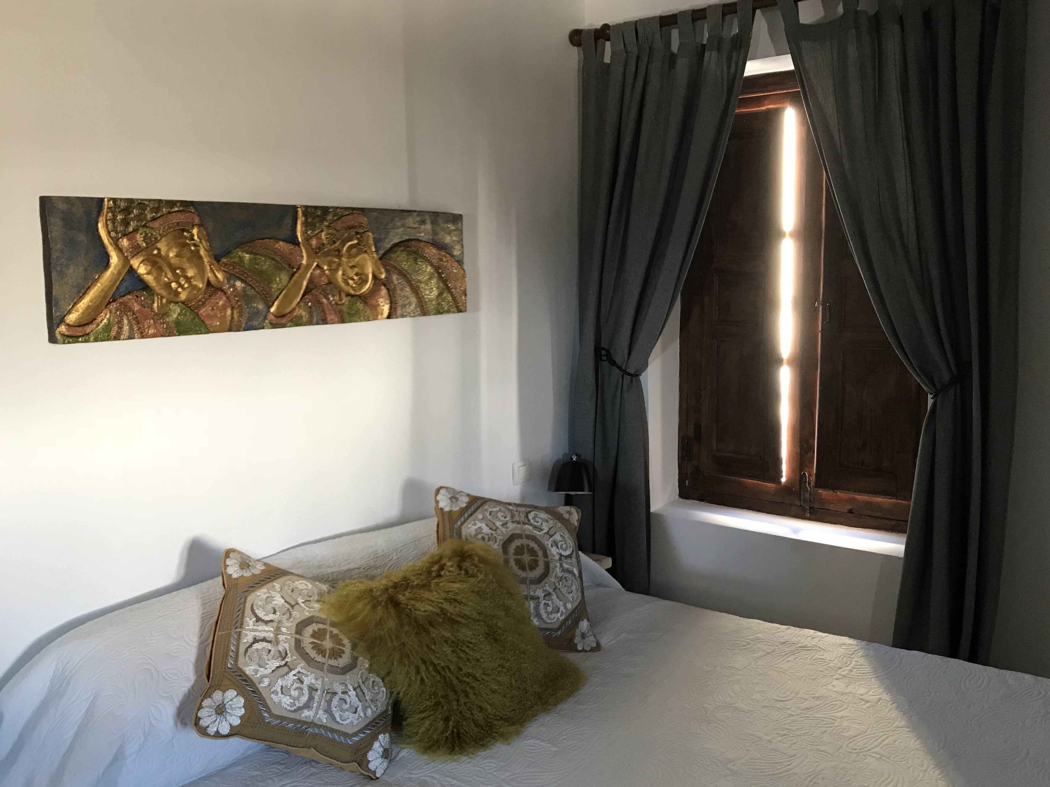 Quarto com cama, janela com cortinas e uma obra de arte pendurada na parede.