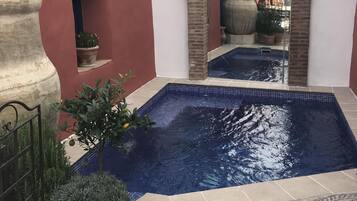 Un patio con piscina, plantas en macetas y suelo de baldosas.